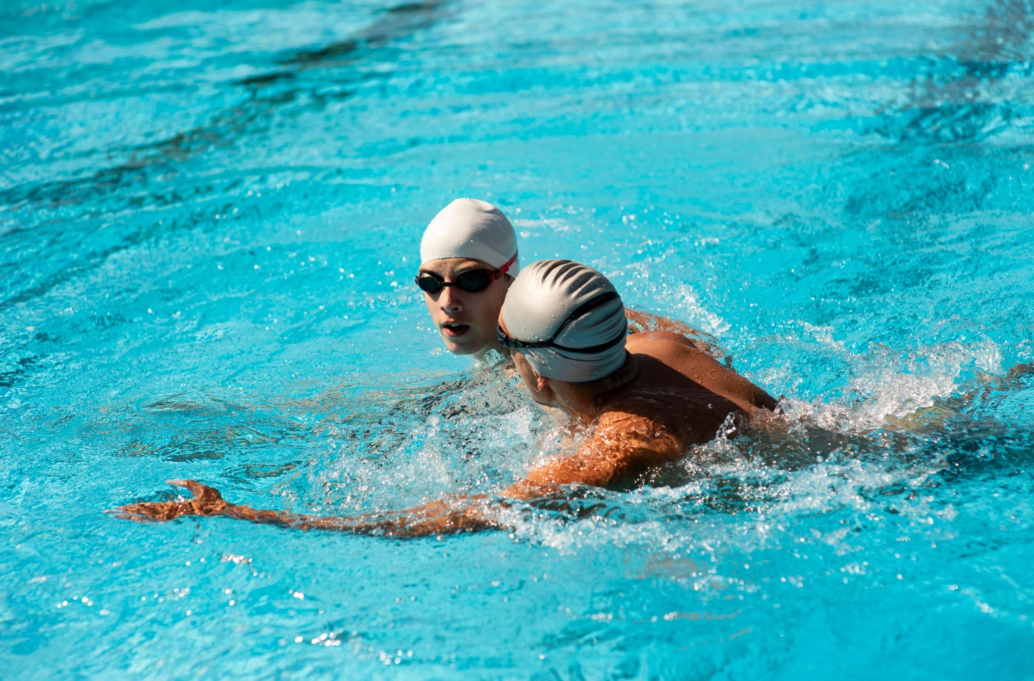 Two swimmers training in a pool wearing swim caps and goggles
