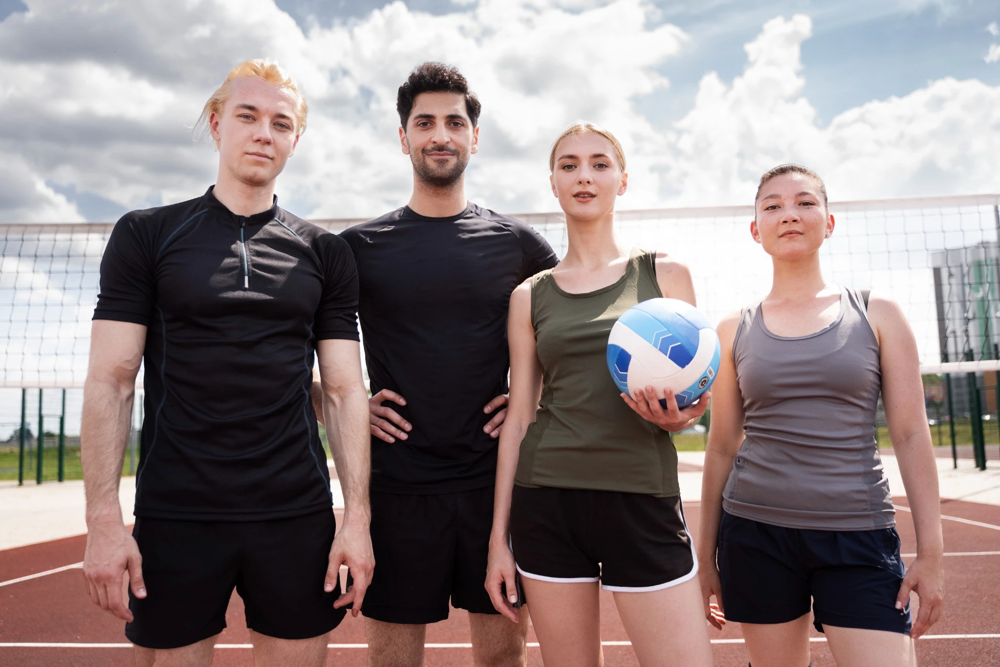 Four athletes standing on an outdoor volleyball court holding a ball before a match
